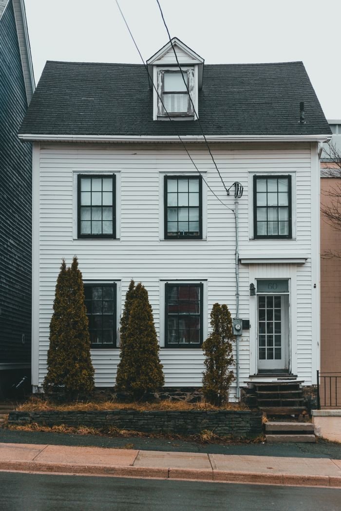 Exterior of white residential building with stairs located near green coniferous trees and sidewalk on street of suburb area in town